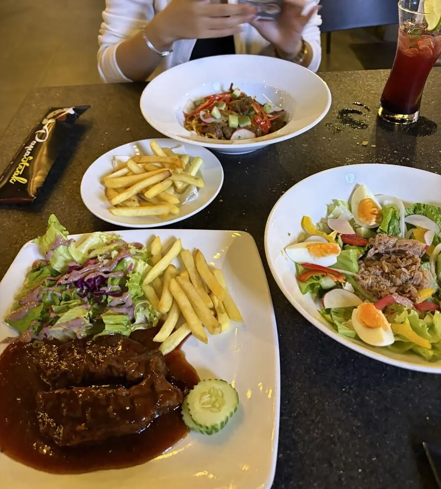 PapaSteakのテーブル、ステーキとサラダ、フライドポテト、麺料理が並ぶ