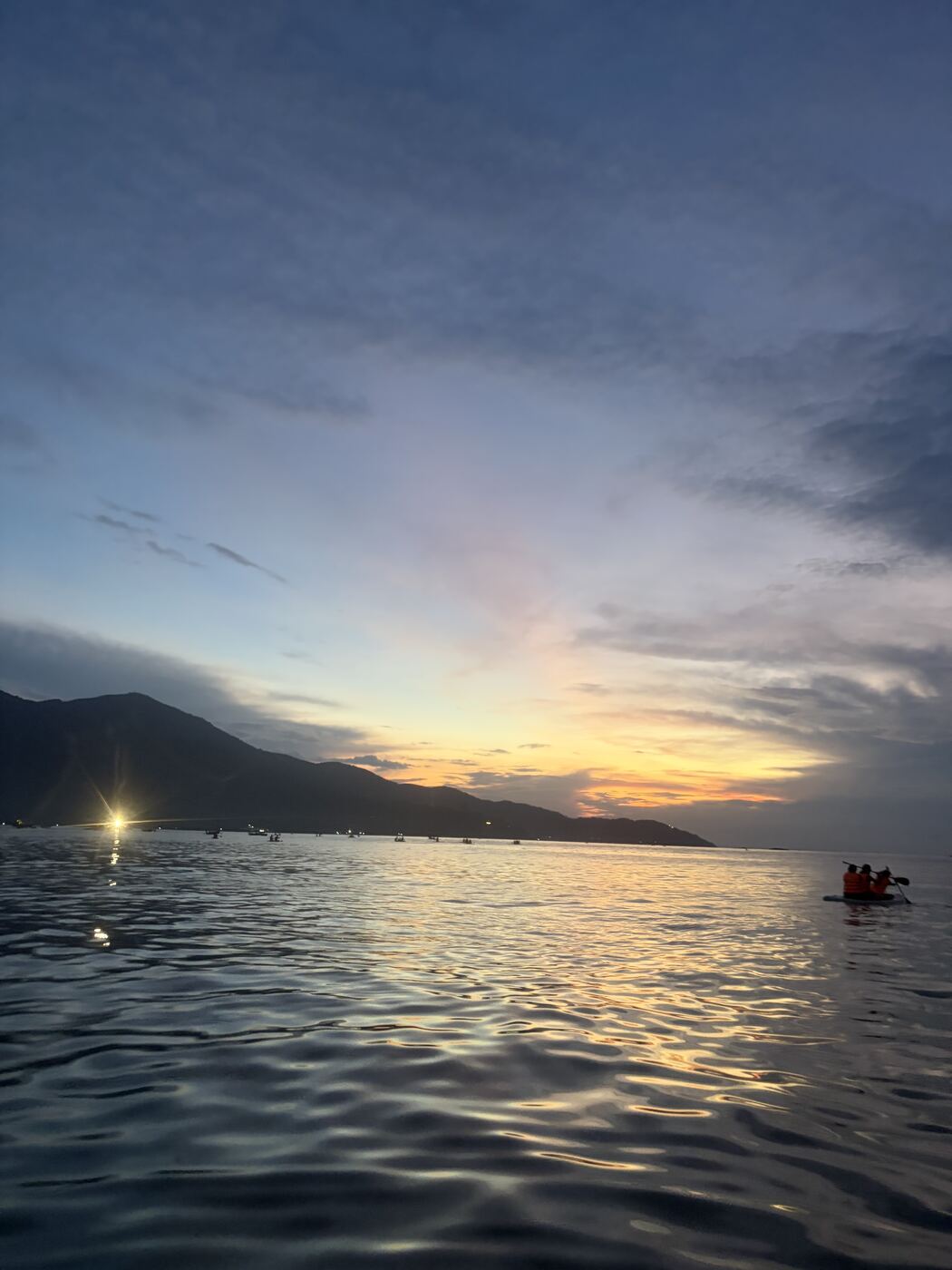日の出前の薄明かりの空と海、SUPを漕ぐ人たちのシルエット